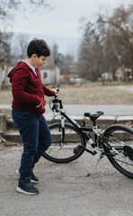 A young kid is standing with his bicycle outdoors in the park, showing a sense of joy and activity.