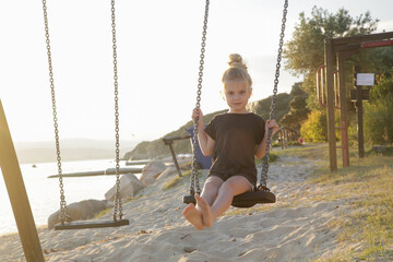 Happy little girl on swing on the sandy beach 