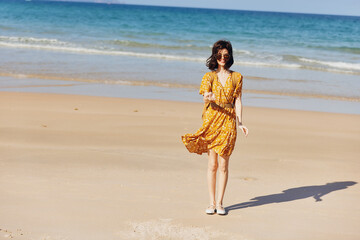 Woman in a vibrant yellow dress standing elegantly on a sandy beach with the vast ocean in the...