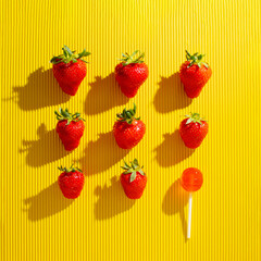 Strawberries pattern against yellow background with one lollipop. Minimal summer fruit concept.