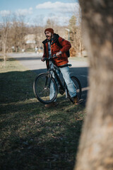 Fototapeta premium Joyful bearded man in casual attire smiling and riding a bicycle on a clear day, showcasing active lifestyle and leisure in a park setting.