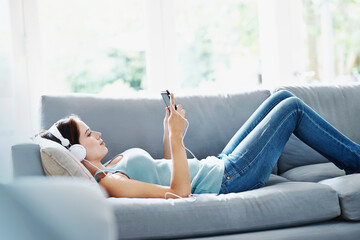 Woman, headphones and phone on sofa in house for music, relax and self care while on study break....