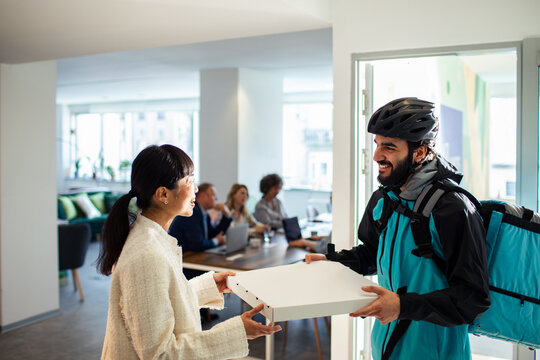 Delivery service courier handing over pizza box to customer in office