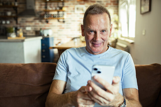 Middle Aged Caucasian man using smartphone on the sofa at home