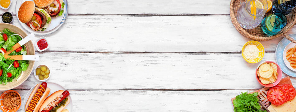Summer BBQ or picnic double border with hamburgers, hotdogs, salad and snacks. Top view over a white wood banner background. Copy space.