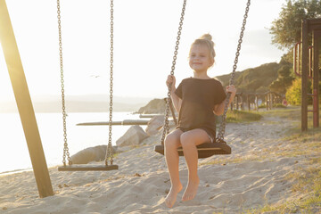 Happy little girl on swing on the sandy beach 