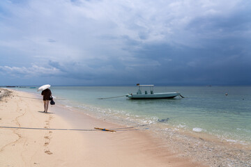 Woman walking sandy beach in Nusa Lembongan, Bali, Indonesia, with umbrella to protect from Sun....