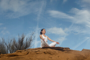 Woman meditating and practicing yoga on top of red rocks, breathing exercises