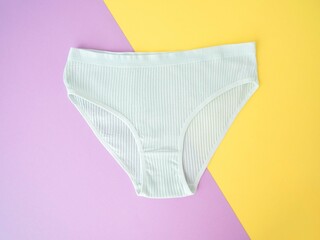 White cotton women's underpants on a purple and yellow background. A piece of clothing for a person. Lingerie