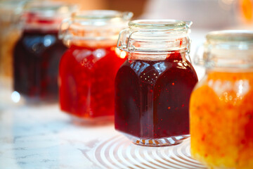 A row of jars with different colored jams. The jars are lined up on a table