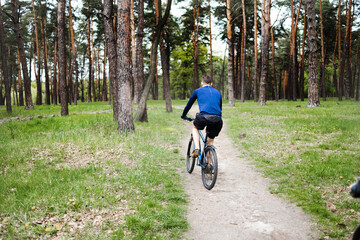 Rear view of young people riding bike in forest on summer day