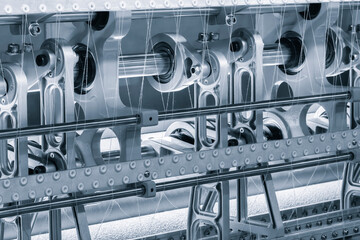 A machine is weaving a fabric with many different colored threads. The machine is blue and white
