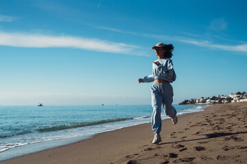 a girl in a sportsuit runs along the seashore. Expressive emotions pleased a woman running along the beach and feeling freedom. Emotions of happiness and pleasure. Happy girl running on the beach