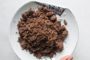 Dark brown sugar in a white plate on a white marble table, sugar for baking in a white plate