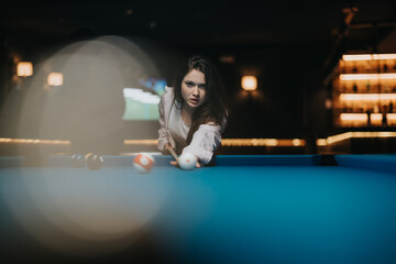 Intense young female concentrating on her pool shot in a dimly lit bar with a modern vibe.