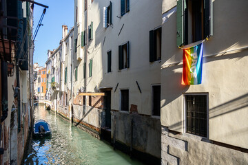 Italian rainbow flag waving from a window by a channel in Venice with Pace (peace) written on it;...