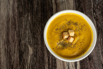 Crema de ayote con crotones, servido en un bowl blanco sobre un fondo de madera. vista superior