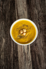 Crema de ayote con crotones, servido en un bowl blanco sobre un fondo de madera. vista superior