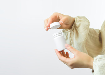 female hands open a white plastic jar with pills on a white background