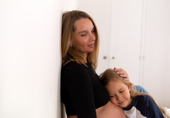 Little cute daughter hugging pregnant mother at home