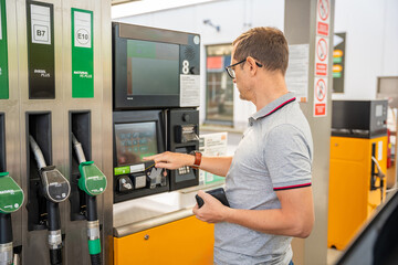 Naklejka na ściany i meble The man pays for fuel with a credit card on terminal of self-service filling station in Europe