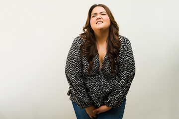 Stressed plus-size woman holding her urge to pee and suffering from incontinence in a studio