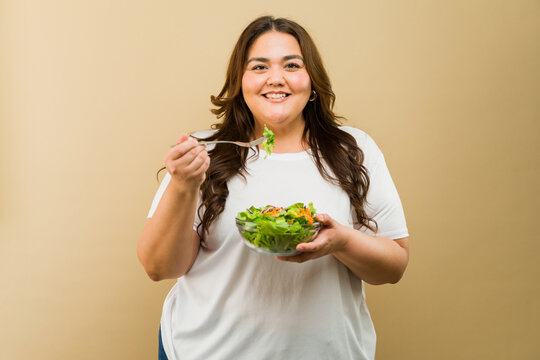 Happy curvy lady enjoying a nutritious salad in a studio