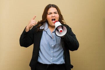 Plus-sized Hispanic businesswoman and boss expressing herself with a megaphone in a studio