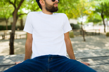 Casual pose of a hispanic man in a plain white t-shirt, perfect for mockup designs, in a sunny park setting