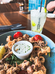 Crispy Fried sea food with lemon, sour cream and cherry tomatoes with green and mayonnaise in the centre of a dish