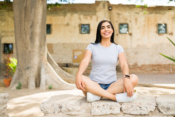 Smiling latin woman in a plain gray t-shirt relaxes outside, ideal for a mockup against a sunny background