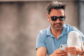 attractive young man with sunglasses looking at his mobile phone on the street outdoors