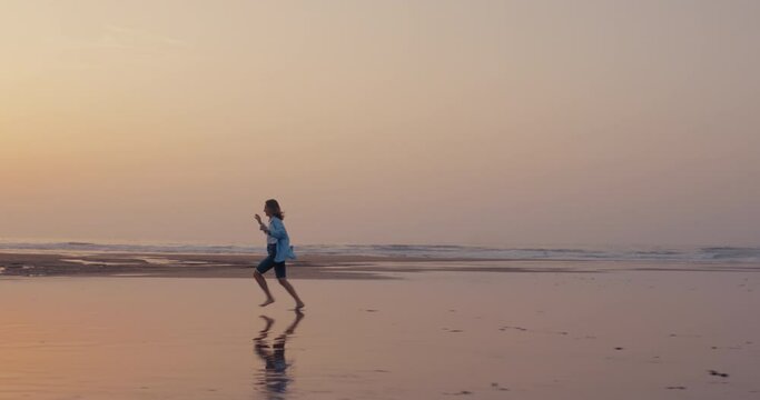 Cinematic commercial shot of woman run wild, young and free on sandy beach during low tide in sunset light. Happy and excited, concept of freedom and happiness. Emotions feelings overload