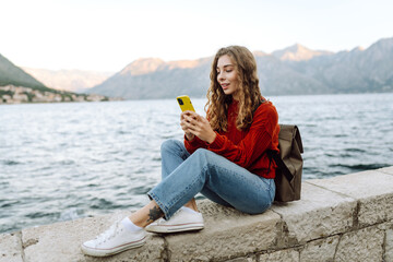 Young woman with phone on the embankment. Tourist during holidays. Lifestyle, travel, nature, active life.