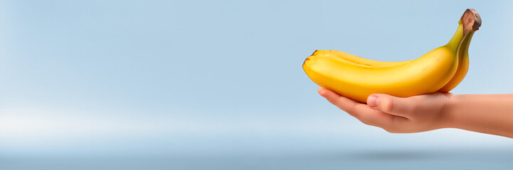 A child's hand holds bananas against a gray-blue background, healthy eating and fruits.Ripe yellow bananas in a child's hand, perfect background for themes of healthy eating and vitamins.