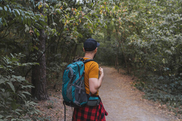 Back view of a young male tourist walking the forest path with big travel backpack