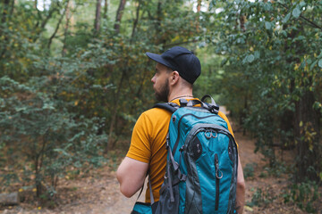 Half-length portrait of a young tourist man walking the forest path with a big travel backpack