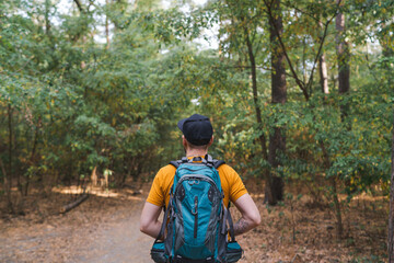 Back view portrait of a young bearded backpacker man walking the forest path