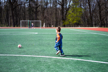 A young boy is playing soccer on a field. He is wearing a blue overalls and is holding a soccer ball
