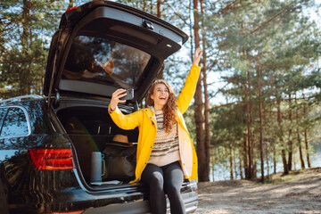 Woman is resting in trunk of car and taking selfie. Lifestyle, travel, tourism, nature, active life.