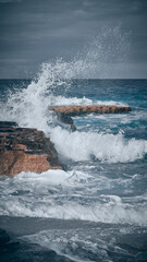 Fototapeta na wymiar Waves of rushing sea are crashing over rocky coastline. Sea waves break upon rocks