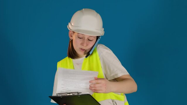 Worried female taskmaster talks via mobile phone reporting about problem on blue background. Woman builder with clipboard consults on call