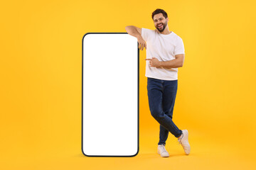 Man pointing at huge mobile phone with empty screen on dark beige background. Mockup for design