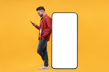 Man with mobile phone standing near huge device with empty screen on orange background. Mockup for...