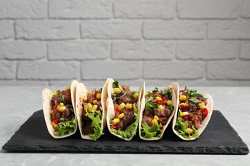 Delicious tacos with meat and vegetables on light gray marble table against brick wall