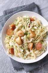 Delicious scallop pasta with spices in bowl on gray textured table, top view