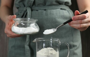 Woman adding baking powder into measuring cup, closeup