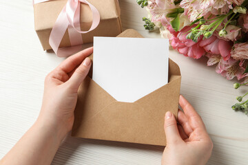 Happy Mother's Day. Woman holding envelope with blank card at white wooden table, top view