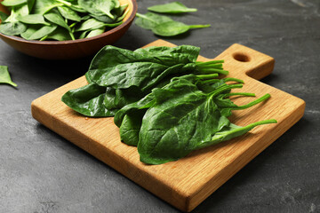 Board with wet fresh spinach leaves on dark textured table, closeup