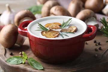 Delicious homemade mushroom soup in ceramic pot and fresh ingredients on wooden table